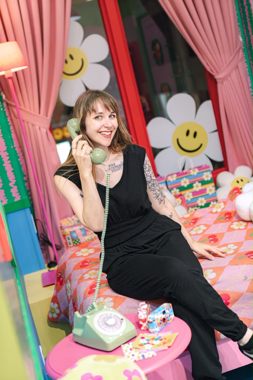 Lena telefoniert lachend in einem bunten Zimmer